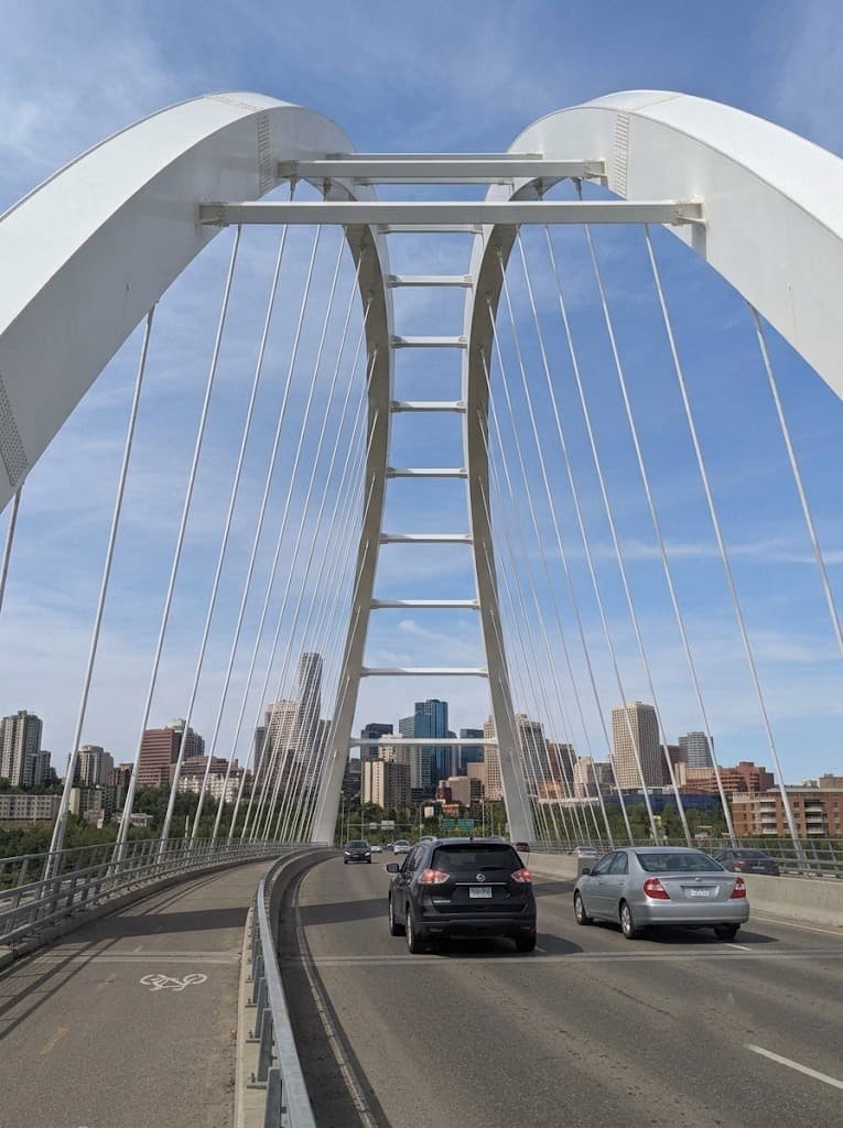 A modern white arch bridge over a river, with a city skyline visible in the background.